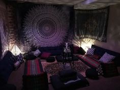 a living room filled with lots of couches and pillows in front of a tapestry