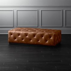 a brown leather bench sitting on top of a hard wood floor next to a wall