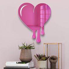 a pink heart shaped wall clock hanging on the side of a wall next to a potted plant