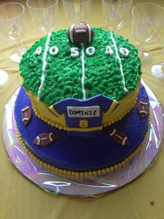 a football themed birthday cake with green frosting and blue icing, on top of a table