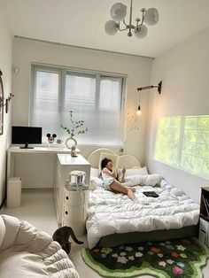 a woman laying on top of a white bed in a bedroom next to a window