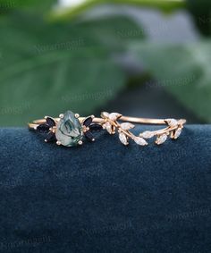 a close up view of a ring with leaves and stones on the front, sitting on a blue velvet surface