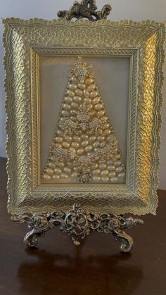 an ornate gold frame with a christmas tree in the center on a wooden table next to a white wall