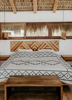 a bed sitting under a wooden roof next to two tables and windows in a room