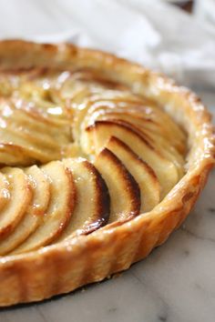 an apple pie with sliced apples on top sitting on a marble countertop, ready to be eaten