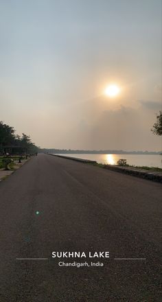 the sun shines brightly in the sky over an empty road by the water at dusk