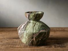 a green marbled vase sitting on top of a wooden table next to a wall