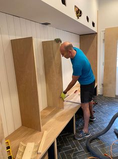 a man sanding wood in a room with tile on the floor and shelves behind him