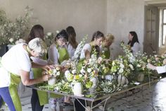 a group of women standing around a table with vases filled with flowers