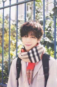 a young man with a scarf around his neck standing in front of a metal fence