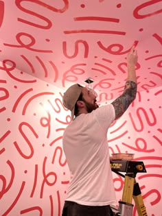 a man with a paintbrush painting the ceiling in red and white letters on a pink wall