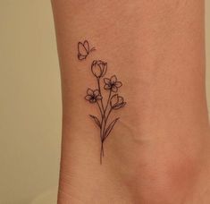 a small flower tattoo on the side of a woman's ankle, with butterflies flying above it