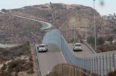 two police cars driving down a road next to a fence and mountains in the background