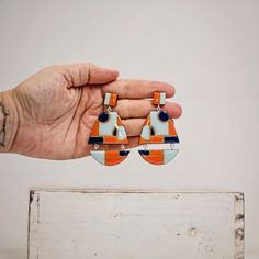 "Large, but light and very elegant statement earrings. Made with wooden elements and finished with epoxy resin. These geometric earrings come in two variations - hypoallergenic silicone studs and metal clip on. You have to choose from variations the type you prefer. The earrings have bright geometric pattern in blue and orange and can be perfect addition to your jewelry collection.  These cool, trendy earrings definitely will brighten your autumn wardrobe. The length of the earrings is 7.0 cm. The clip ons does not contain nickel. Please keep in mind that colors may vary slightly from those viewed on your monitor. Please see \"Shop Policies\" section for more important information about shipping, refunds, custom options and more. CARE INSTRUCTIONS - store in a clean, dry place. Use of oils Bold Orange Drop Earrings, Modern Orange Drop Earrings, Modern Blue Geometric Earrings, Handmade Blue Geometric Earrings, Homemade Earrings, Autumn Wardrobe, Colorful Earrings, Trendy Earrings, Blue And Orange