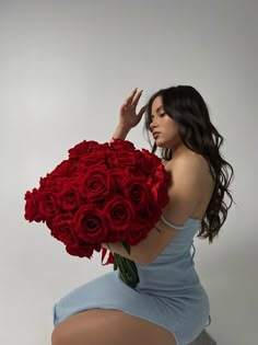 a woman holding a bunch of red roses in her hand and sitting on the ground