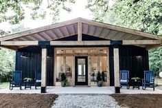 a small black cabin with blue chairs on the front porch and side entry to it