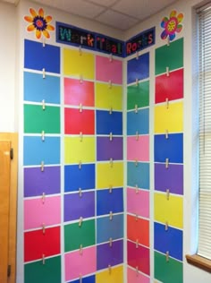 a colorful bulletin board with clothes pins attached to it and flowers on the back wall