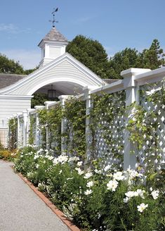 a white picket fence with flowers in the foreground and a house in the background