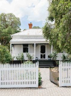 a white picket fence in front of a house with trees and bushes on the side