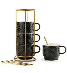 a set of four black and gold coffee mugs with spoons in front of them