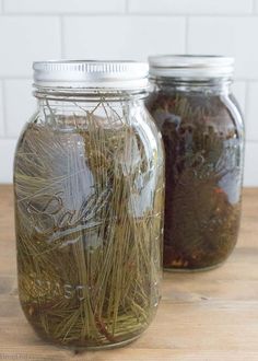 two mason jars filled with grass on top of a wooden table