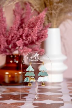 a pair of earrings is displayed in front of a vase with pink flowers on it