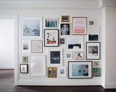 a wall with many pictures on it in a room that has wood floors and white walls