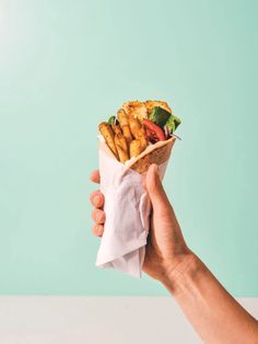 a hand holding a wrap filled with fried chicken and veggies on a blue background