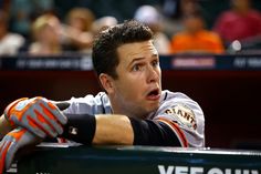 a baseball player sitting in the dugout with his hand on his hip and looking at something