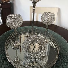 a clock sitting on top of a glass table next to two candlesticks and a mirror