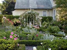 the garden is full of beautiful flowers and greenery in front of a white house