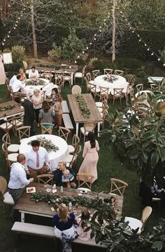 a group of people sitting at wooden tables in the middle of a yard with string lights