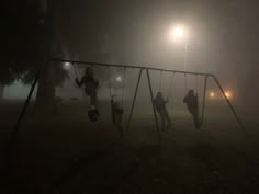 children playing on a swing set in the fog at night with street lights behind them