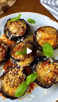 a white plate topped with stuffed eggplant covered in cheese and herbs on top of a wooden table