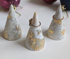 three white and gold decorated christmas trees on a table with ornaments in the back ground