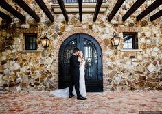 a bride and groom standing in front of a stone building