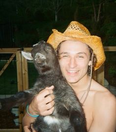 a man wearing a straw hat holding a baby goat in his arms and smiling at the camera