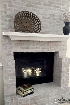 a white brick fireplace with candles on top and some books in the corner next to it