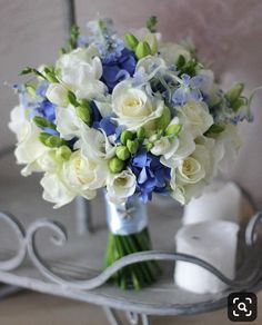 a bouquet of white and blue flowers in a vase on a metal stand next to a mirror