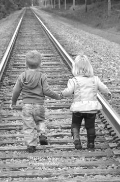 two children walking on train tracks holding hands