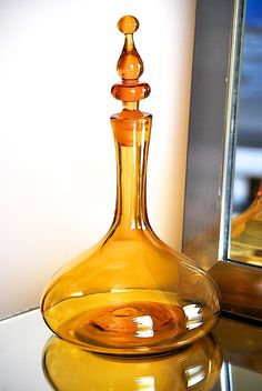 a yellow glass bottle sitting on top of a table next to a mirror and vase