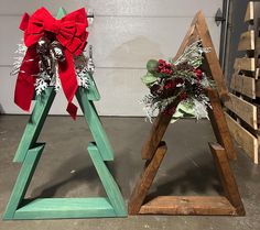 two wooden christmas trees with red bows and greenery on them, sitting next to each other