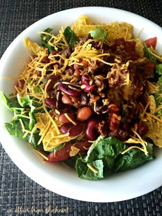 a salad with beans, cheese and lettuce in a white bowl