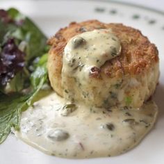 a white plate topped with meat patties covered in gravy next to a salad