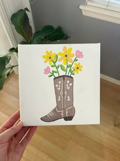 a hand holding up a card with flowers in a cowboy boot