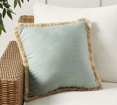 a close up of a pillow on a couch with a plant in the back ground