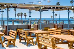 an outdoor dining area with wooden tables and benches overlooking the ocean in front of palm trees