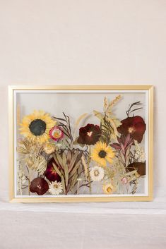 an arrangement of flowers is displayed in a gold frame on a white tableclothed surface