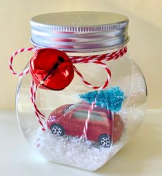 a glass jar with a red car and a blue christmas tree in it sitting on top of snow