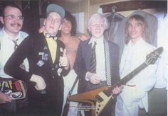 a group of men standing next to each other holding guitars and giving the thumbs up